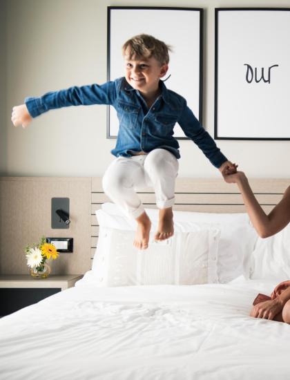 Bambino salta sul letto, donna sorride, decorazione accogliente.