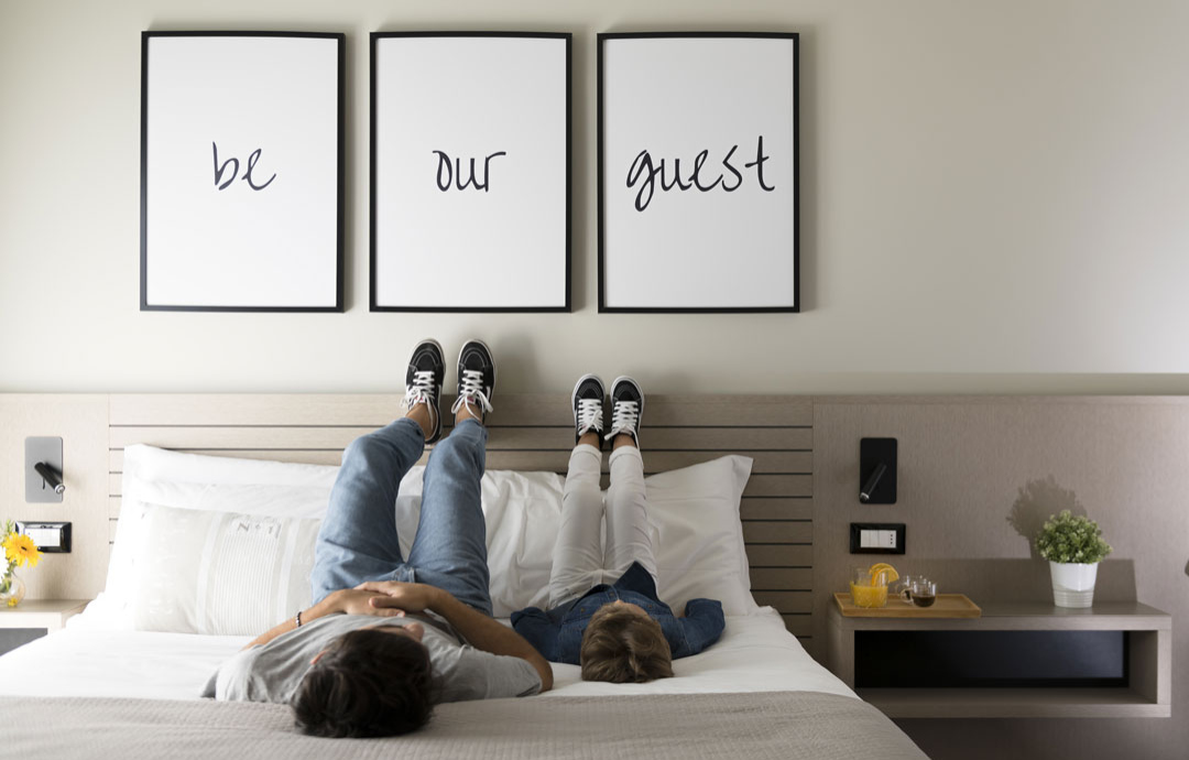Two people on a bed with 'be our guest' frames above.